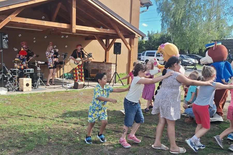 Děti tančí s maskoty před pódiem, na kterém hraje kapela P.O.R.T.